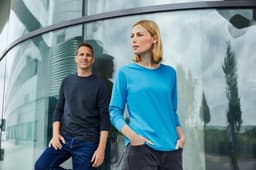 A promotional image featuring a man in a dark shirt and a woman in a blue long-sleeve T-shirt, both standing outdoors.