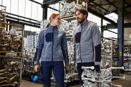 A grey fleece jacket with contrasting navy and red accents, featuring a logo, worn by two people in a warehouse setting.