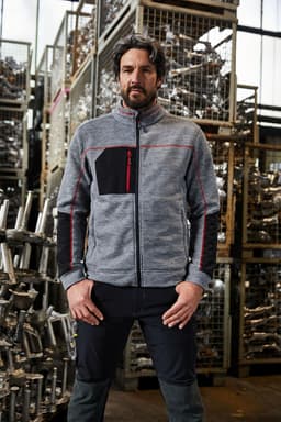 A grey and black polar fleece jacket with a zippered front and a chest pocket, displayed in an industrial setting.
