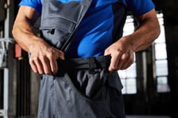 Workwear pants with bib in dark grey, featuring pockets and adjustable straps, being worn by a person.