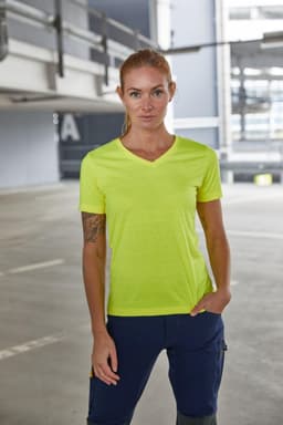 A vibrant yellow ladies work t-shirt, featuring a v-neck design, displayed in an industrial setting.