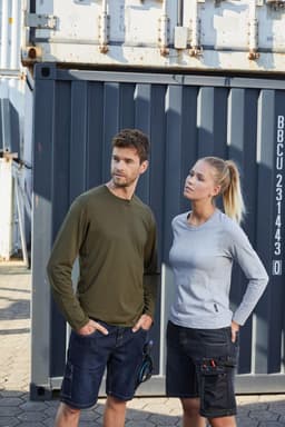 A grey long-sleeve women's work T-shirt is paired with a green long-sleeve men's T-shirt against a shipping container backdrop.