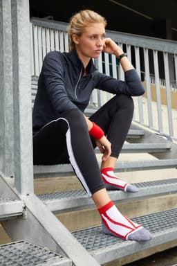 A pair of red and grey sneaker socks worn by a woman sitting on metal stairs, dressed in athletic wear.
