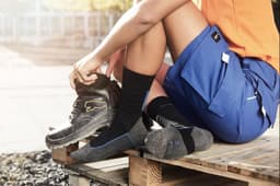 Worker socks in black and grey worn with work boots, paired with shorts, on a wooden pallet outdoors.