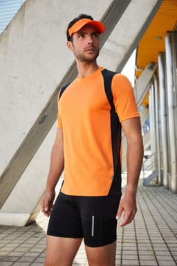 A man in a fluorescent yellow and black running T-shirt, paired with black shorts and a visor, stands outdoors.