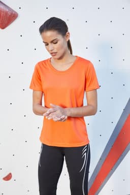 An orange ladies active T-shirt displayed on a model, paired with black athletic leggings. The shirt has a minimalist design.