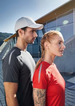 A grey sports T-shirt on a man and a red sports T-shirt on a woman, both with reflective details and a cap.