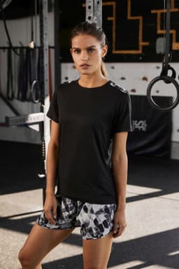 A ladies' black sports shirt displayed with patterned shorts, set against a gym backdrop with equipment.