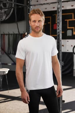 Men's sports shirt in white, featuring a logo, styled with black athletic leggings in a gym setting.