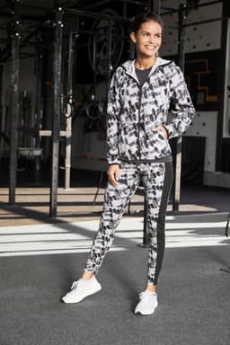 A ladies’ sports jacket in a black and grey abstract pattern, featuring a logo, paired with matching leggings.