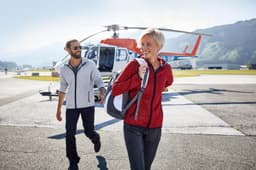 A grey and a red men's knitted fleece hoodie are worn by two people near a helicopter on a tarmac.