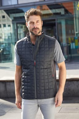 A man wears a charcoal knitted hybrid vest, featuring a quilted design and a zipper, set against a modern urban backdrop.