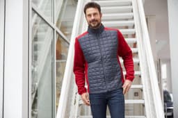 A knitted hybrid jacket featuring red sleeves and a grey quilted front, with a zippered closure and a logo.