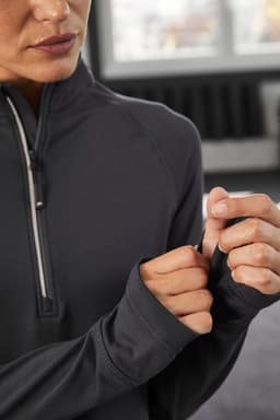 A close-up of a woman wearing a black half-zip sports shirt, showcasing the sleeves and zipper detail.