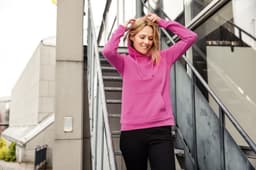 A pink ladies hoodie with a drawstring hood, worn by a woman, against an urban backdrop of stairs and buildings.