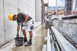 Workwear Bermudas in white, worn by a worker mixing material at a construction site, with a hard hat and tools.
