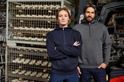 A navy half zip hoodie on a woman and a grey half zip hoodie on a man, both standing in a warehouse setting.