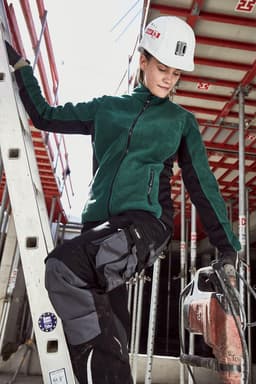 A green polar fleece jacket with black accents, worn by a woman on a ladder at a construction site.