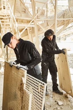 A polar fleece jacket in black, worn by a woman working on a construction site, featuring a logo on the sleeve.