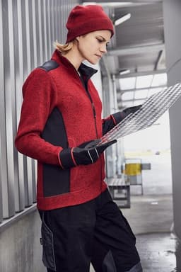 A red knitted fleece jacket with black accents, worn by a person reviewing documents in an industrial setting.