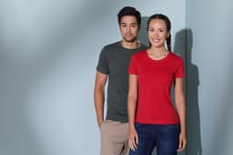 A grey men's T-shirt and a red women's T-shirt on models standing against a light blue background. Both shirts have logos.