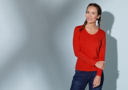A red long-sleeve stretch shirt worn by a model, accompanied by blue jeans. The shirt has a logo.