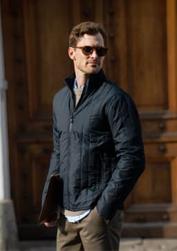 A black soft shell jacket worn by a man holding a laptop case, set against a rustic wooden backdrop.