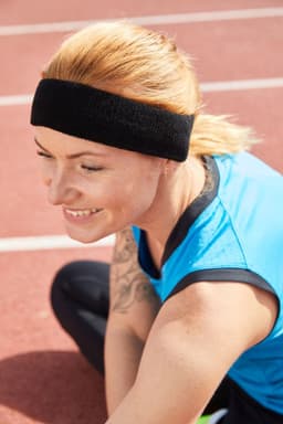 A black Terry headband worn by a woman with blonde hair, seated on a track. She is wearing a blue athletic top.