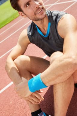 A close-up of a man wearing a blue Terry Wristband on a running track, seated and smiling. He’s in athletic wear.