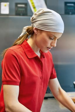 A woman with a white scarf tied back is wearing a red polo shirt while working in a kitchen setting.