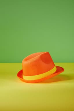 An orange hat with a yellow band, resting on a green and yellow background. It has a mesh design.