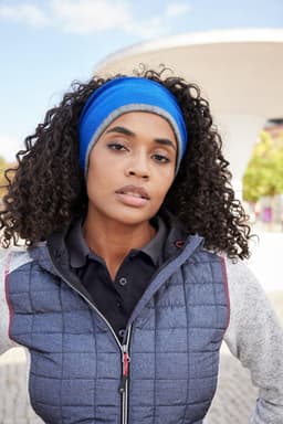 A reversible headband in blue worn by a woman with curly hair, set against an outdoor background.