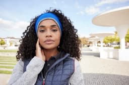 A woman with curly hair is wearing a blue reversible headband and a grey vest in an outdoor setting.