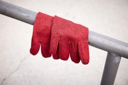A pair of red fleece gloves resting on a metallic railing. The gloves have a textured, knitted appearance.