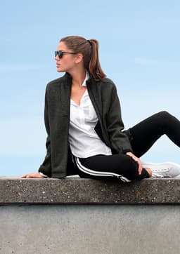 A polar fleece jacket in dark grey worn by a woman sitting casually. It features a logo and is paired with sporty attire.