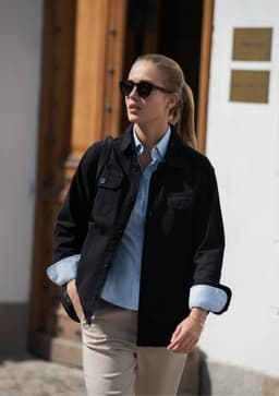 A unisex shirt in black, paired with a light blue shirt underneath, worn with sunglasses outdoors.