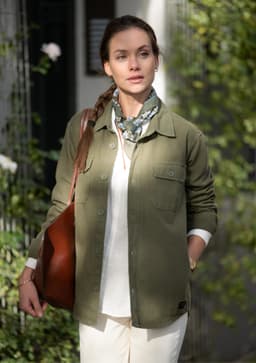 A unisex olive-green shirt with two front pockets, worn over a white top, paired with a patterned scarf and brown bag.