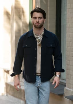 A unisex shirt in navy with buttons, worn over a beige top, paired with light jeans. The model is walking outdoors.