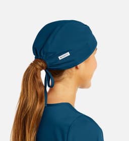 A unisex scrub cap in deep teal, featuring a tied design and a small branded label.