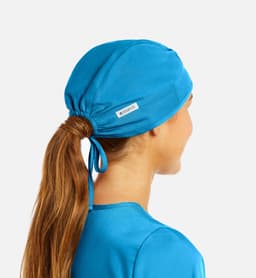A unisex scrub cap in vibrant blue, designed with a ponytail opening at the back. Features a logo tag.