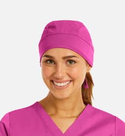 A unisex scrub cap in bright pink, worn by a smiling woman in a matching scrub top. The cap features a logo.