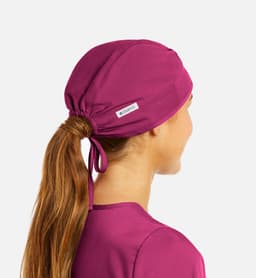 A unisex scrub cap in a vibrant fuchsia colour, featuring a logo and a ponytail opening at the back.