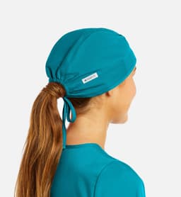 A unisex scrub cap in teal with a gathered ponytail opening and a small logo tag.