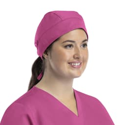 A unisex pink scrub cap with buttons, worn by a smiling woman in a scrub top.