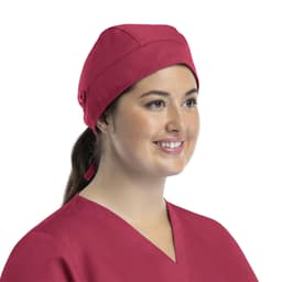 A unisex scrub cap in a vibrant pink colour, featuring buttons and a structured design, worn by a smiling individual.