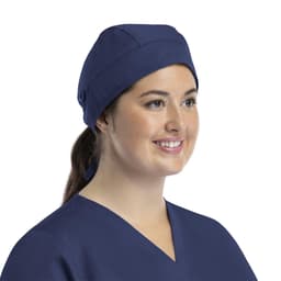 A unisex navy scrub cap with buttons, worn by a woman with long hair tied back, smiling while wearing scrubs.