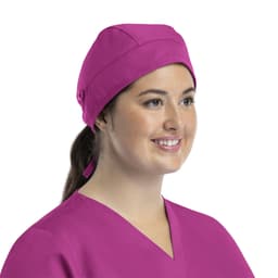 A unisex scrub cap in bright pink with buttons, worn by a woman smiling. It features a stylish design.