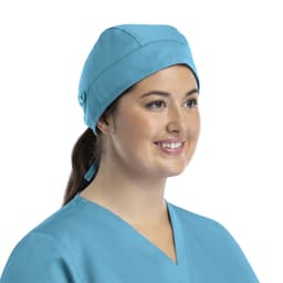 A unisex scrub cap in light blue with buttons, worn by a person with a ponytail, smiling.