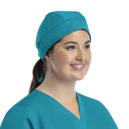A unisex scrub cap in a vibrant turquoise colour with buttons, worn by a smiling individual.