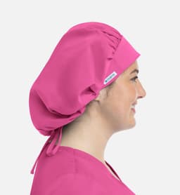 A unisex bouffant cap in bright pink, worn by a smiling person, featuring a logo on the side.